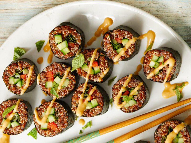 quinoa sushi rolls on a white plate, drizzled with thai peanut sauce, two chopsticks set on the plate