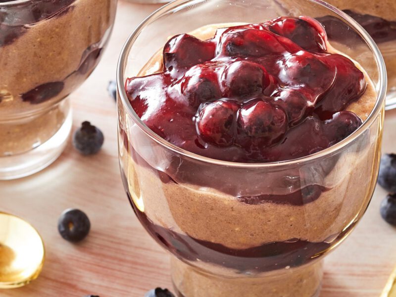 Creamy Blueberry Parfaits with Millet in glass parfait glasses next to three gold spoons and numerous fresh blueberries
