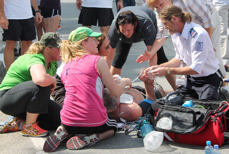 An EMS team surrounds a man lying on the ground having a cardiac arrest