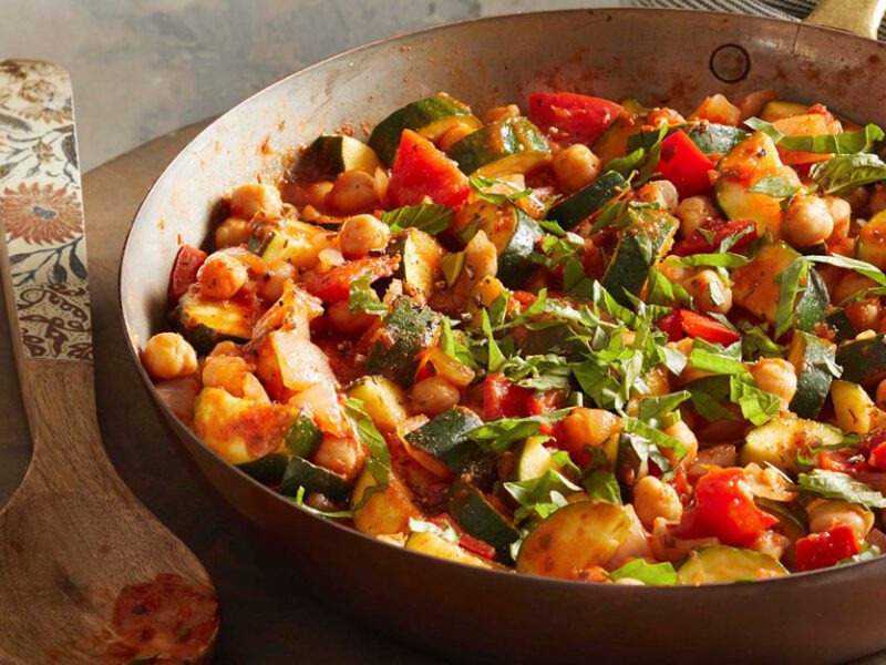Chickpea Zucchini Saute in a large frying pan on a round wooden chopping board with a wooden serving spoon