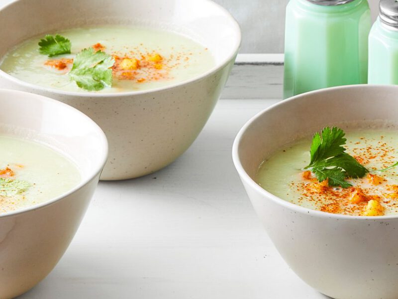 Three bowls of pale green-hued Chayote Soup with Roasted Hominy in white bowls