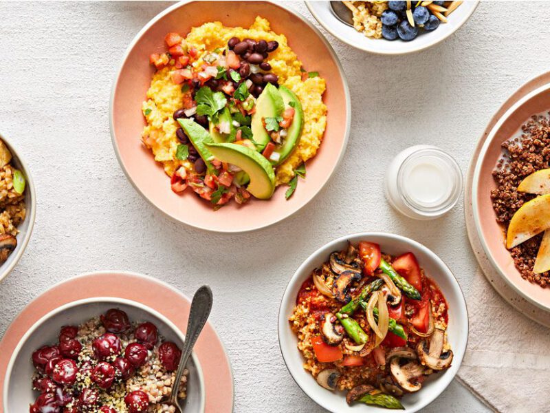 A top-down shot of a white tablecloth topped with six colorful vegan breakfast bowls