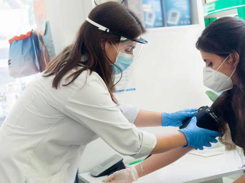 Doctor takes young woman's blood pressure while wearing a mask - COVID-19