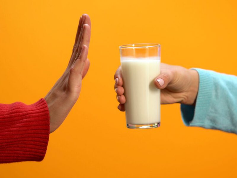 One hand offers a glass of milk, while another hand has its palm vertical in the stop motion