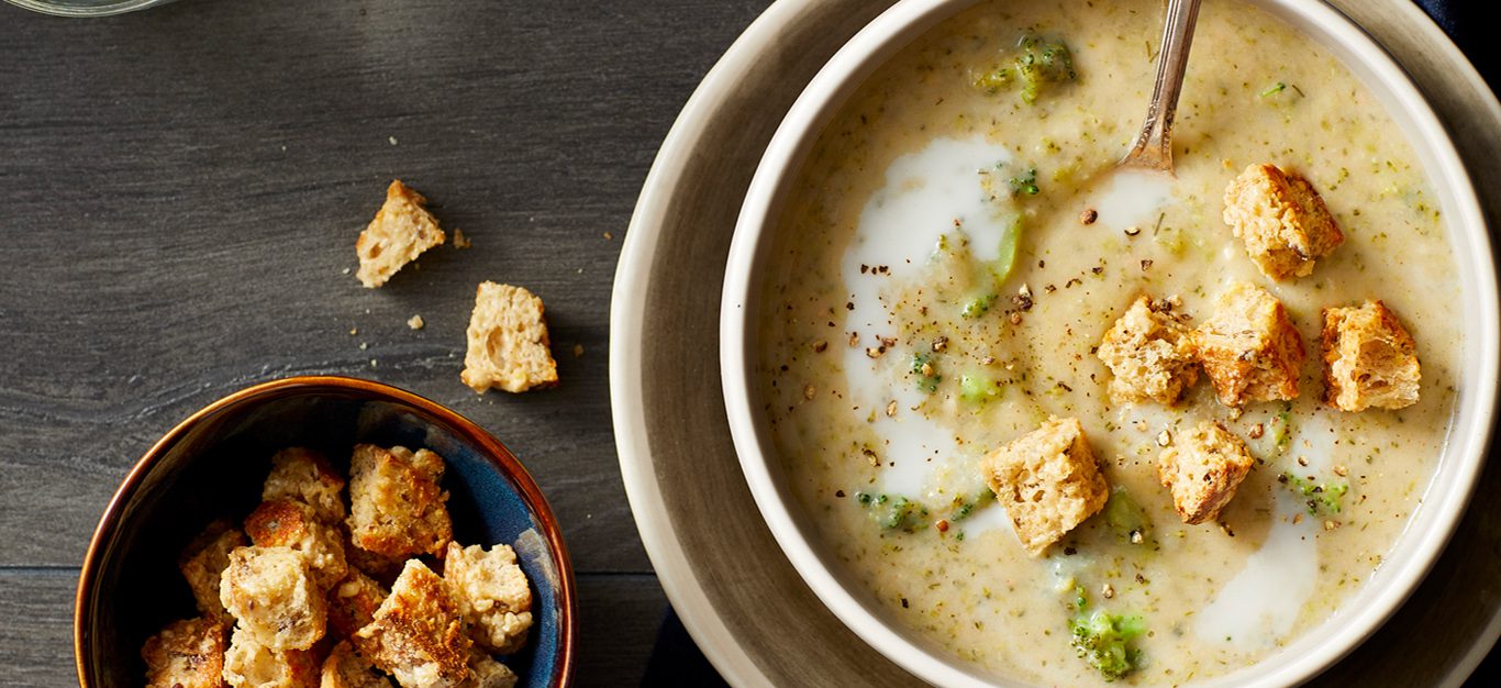 Creamy Broccoli Chowder Soup shown on dark table with a bowl of toasted croutons on the side