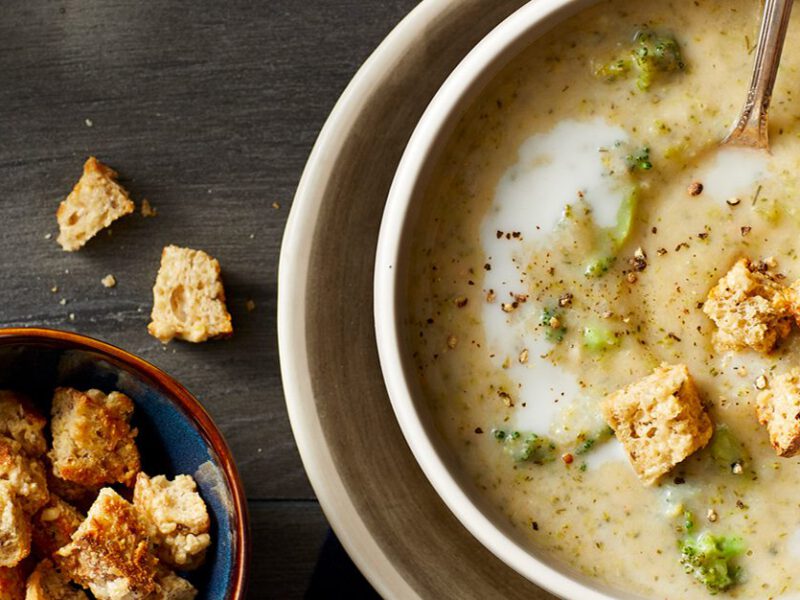 Creamy Broccoli Chowder Soup shown on dark table with a bowl of toasted croutons on the side
