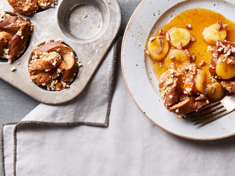 Crispy French Toast Cups with Bananas Foster Topping on a plate next to a muffin tray filled with the mixture, one serve per muffin tray