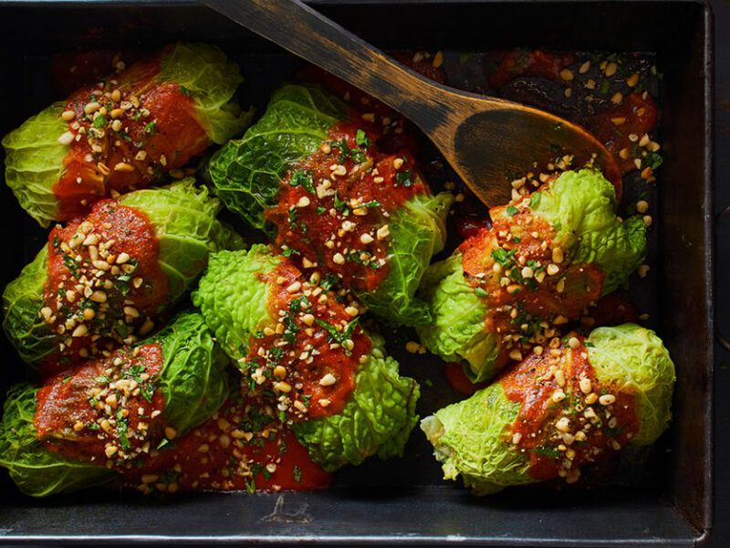 Savoy Cabbage Rolls in a casserole dish drizzled with tomato sauce and sprinkled with tomato sauce while a wooden spoon rests inside the dish