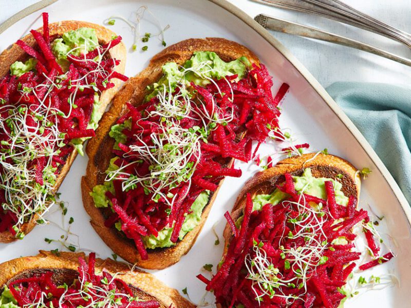 Vegan tartines - toast topped with avocado and bright beets and seasoned with ginger and wasabi, shown on a white plate