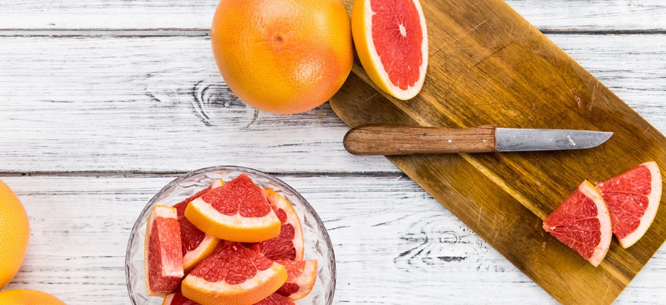 Grapefruit shown sliced into small pieces on a cutting board with a knife