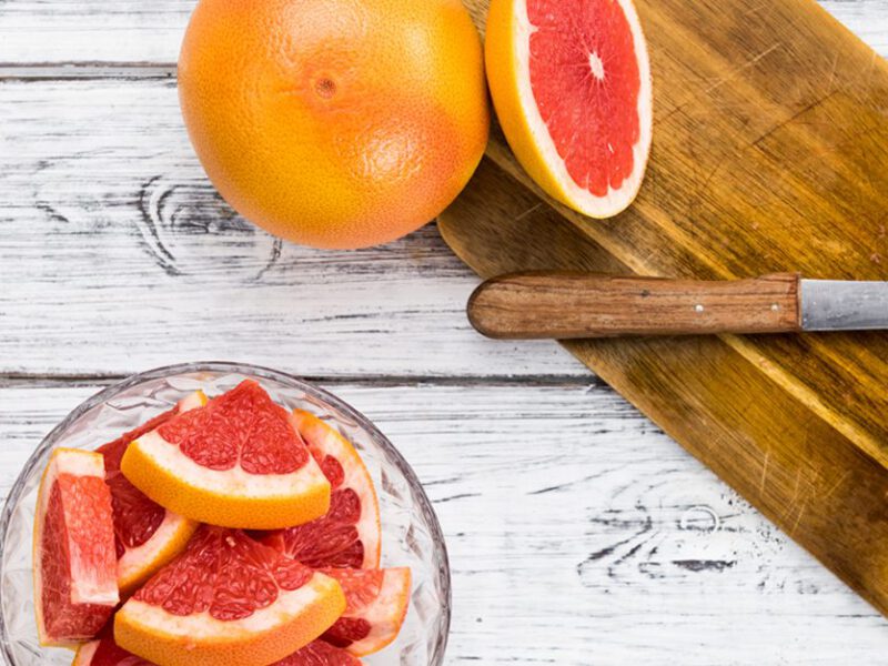 Grapefruit shown sliced into small pieces on a cutting board with a knife