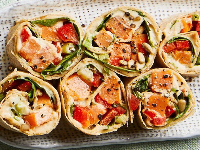 Sliced veggie roll-ups shown from the top down, stuffed with spinach, sweet potato, hummus, and roasted red bell pepper
