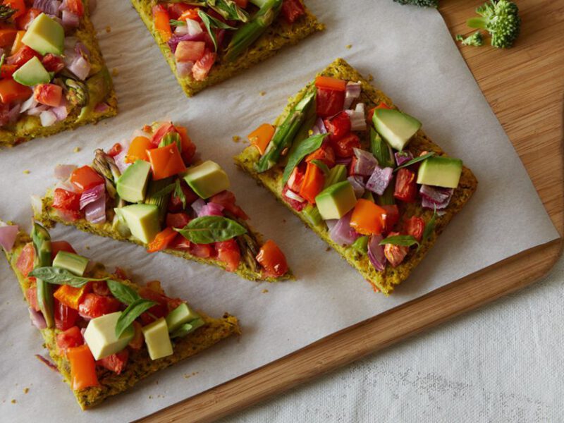 square-cut pizza loaded with veggies including asparagus, tomato, and avocado, with a mildly green crust made of broccoli