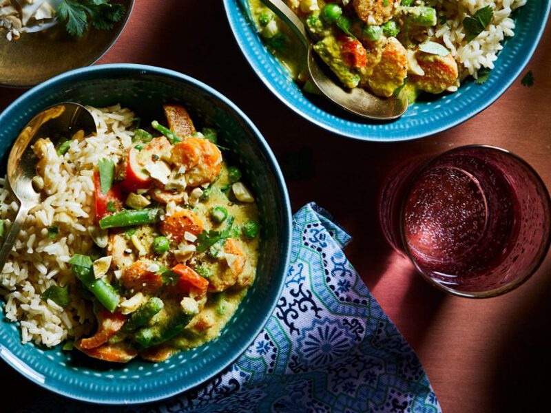A medley of veggies including chopped green beans is shown in a warmly spiced vegan korma sauce with a bed of whole grains