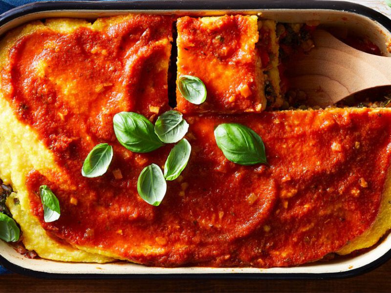 polenta lasagna casserole shown topped with marinara sauce and fresh basil leaves