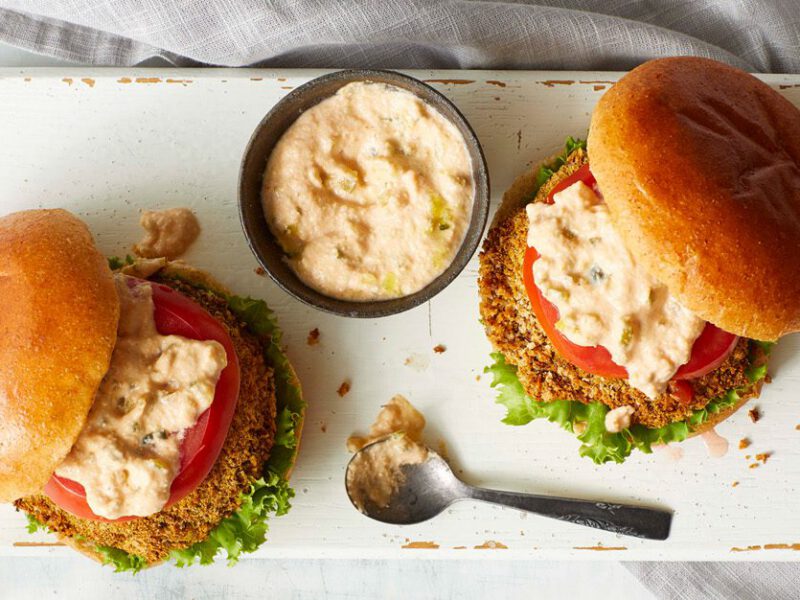Two breaded air-fryer portobello burgers shown from above, drizzled with Thousand Island dressing, which is also in a ramekin between the burgers