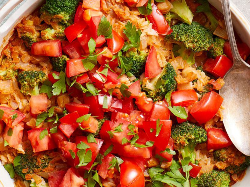 brown rice casserole with broccoli and tomatoes, shown in a round white casserole dish