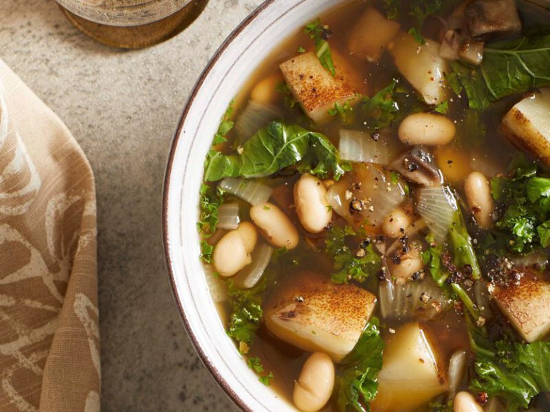 a bowl of minestrone with a thick broth, kale leaves, and chopped potatoes and white beans visible in soup