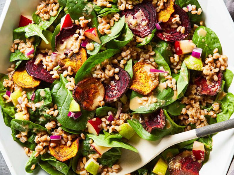 Crispy air fryer beets sit atop a colorful green salad with spinach and other chopped veggies including fresh pair, in a hexagonal white bowl in bright light