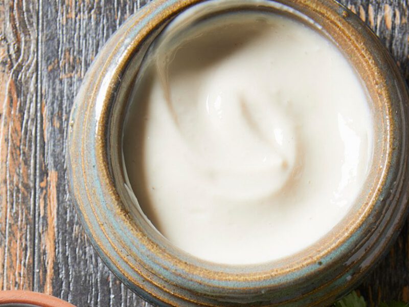 Vegan, plant-based mayo - light, fluffy looking white vegan mayo in a jar, shown from above, sitting atop a gray wooden table