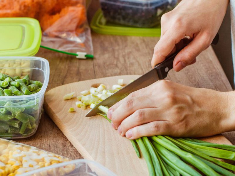 Woman chopping scallions on a wooden cutting board, with plastic tupperware containers beside for meal prep