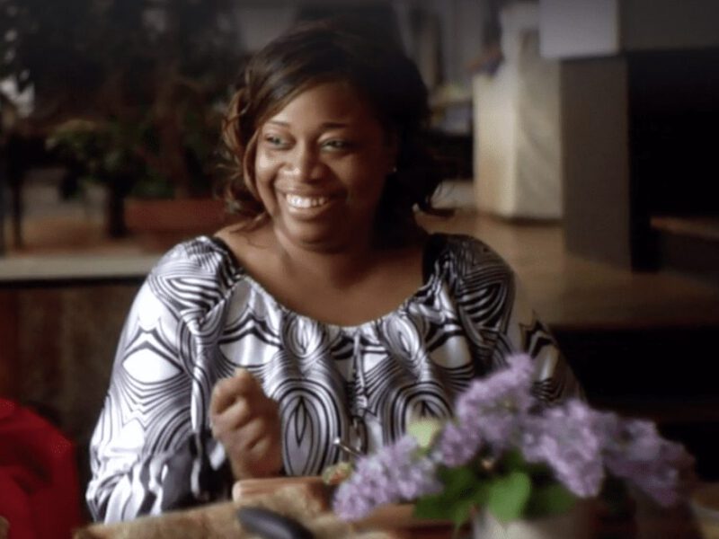 African American woman from the FOK movie in her home looking happy