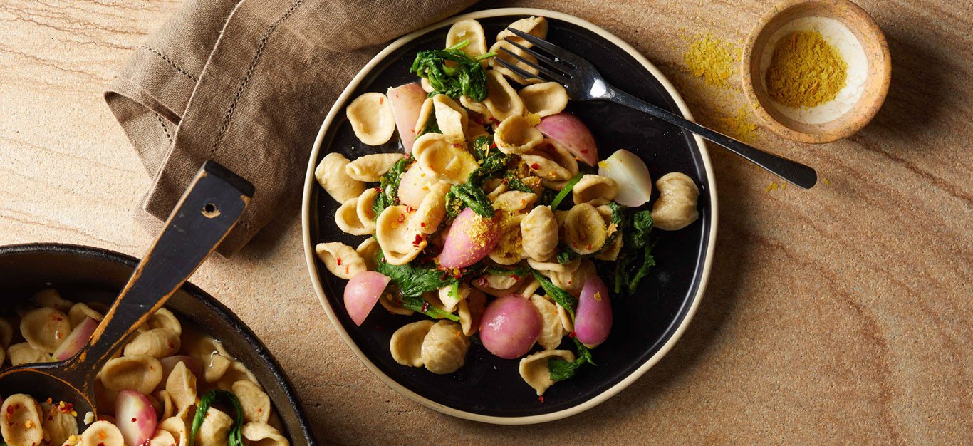 Vegan pasta dish with radish shown on a black plate on a wooden table