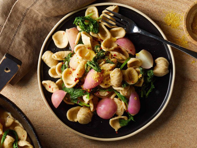 Vegan pasta dish with radish shown on a black plate on a wooden table