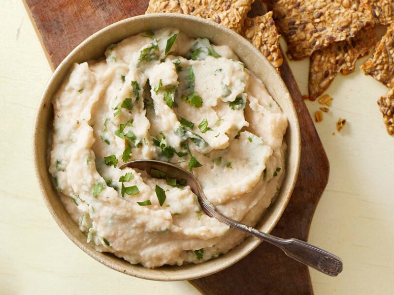 Navy Bean Homemade Hummus - white creamy hummus in a small bowl, garnished with cilantro, with whole grain crackers on the side