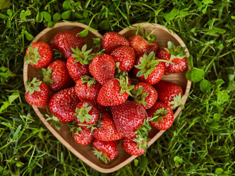 A heart-shaped bowl of strawberries set on green grass