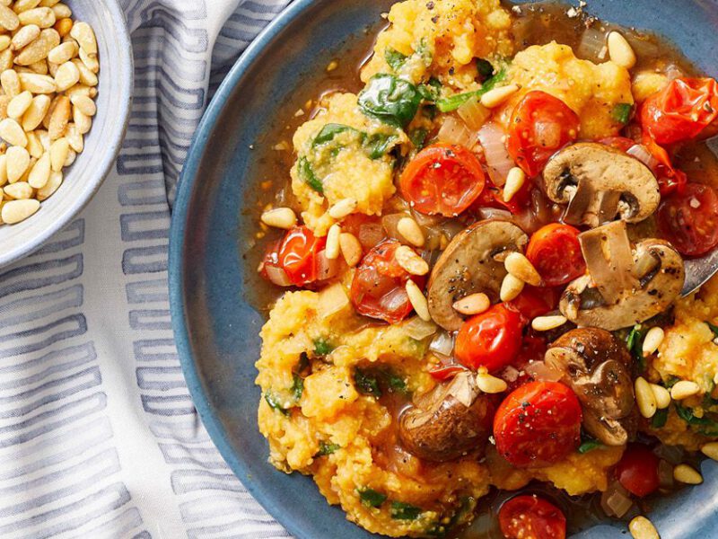 A hearty, colorful bowl of polenta and mashed sweet potato topped with blistered cherry tomatoes and juicy cremini mushrooms, with a dish of pine nuts on the side