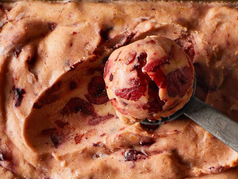 Close-up shot of pink-hued almond cherry nice cream, with visible bits of cherries, and an ice cream scoop