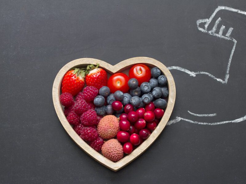 Bowl of fruit sitting atop chalkboard background, with a flexing arm drawn in chalk extending from the bowl of fruit