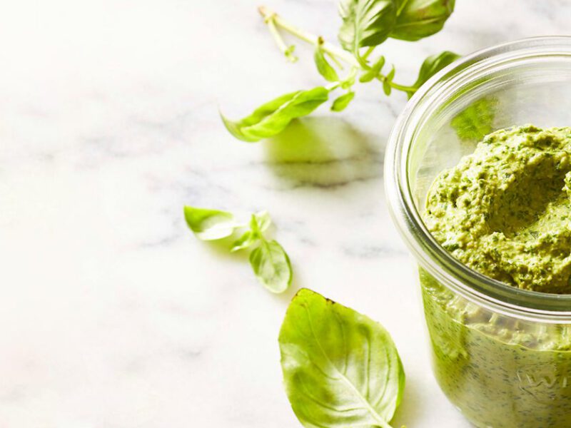 Homemade Vegan Pesto in a glass jar on a white marble table