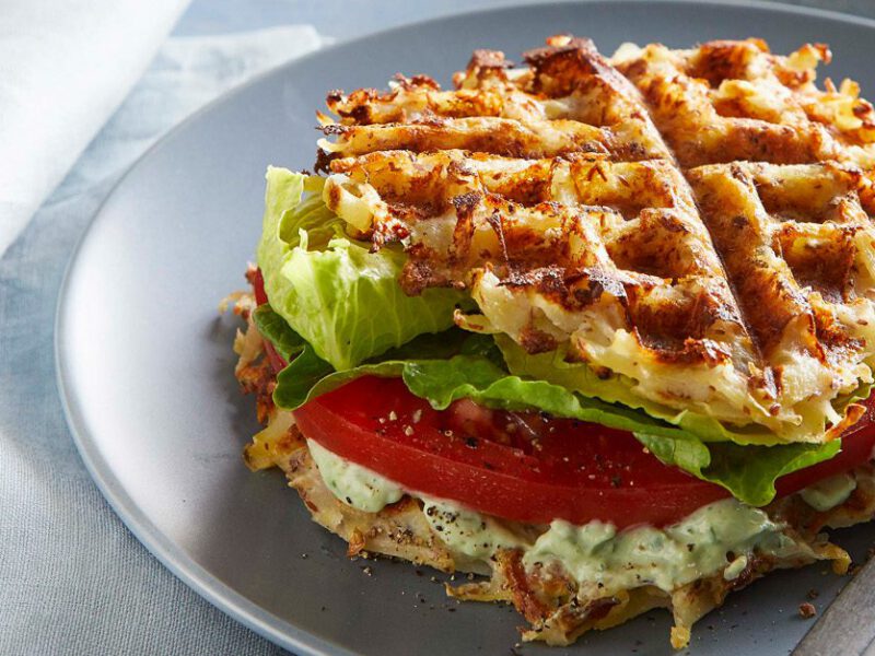 potato waffle sandwiches with lettuce, tomato, and herbed tofu cream on a gray plate with a fork