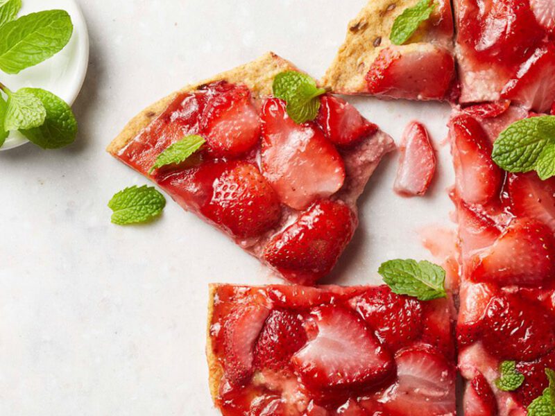 Strawberry Dessert Pizza sprinkled with fresh mint leaves on a white marble countertop