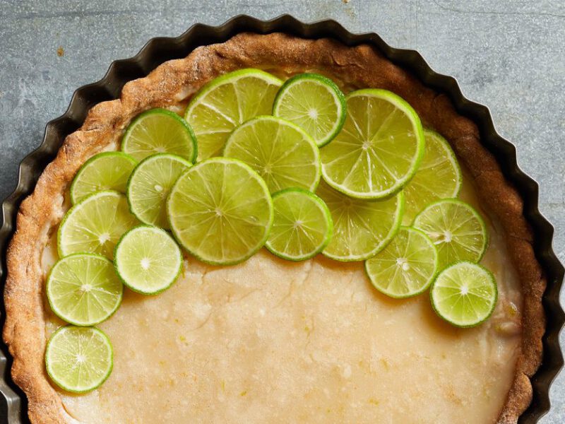 Vegan Key Lime Pie with fresh lime slices in a tart tin on gray marble counter