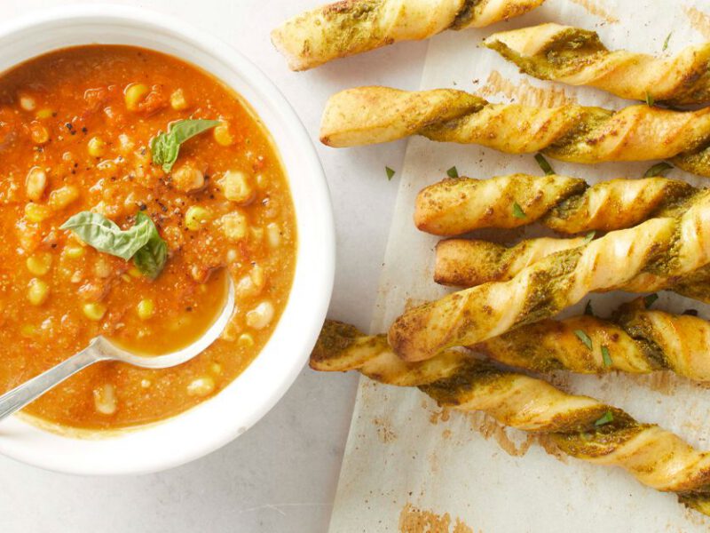 A bowl of Summer Tomato Soup with Pesto Breadsticks on the side
