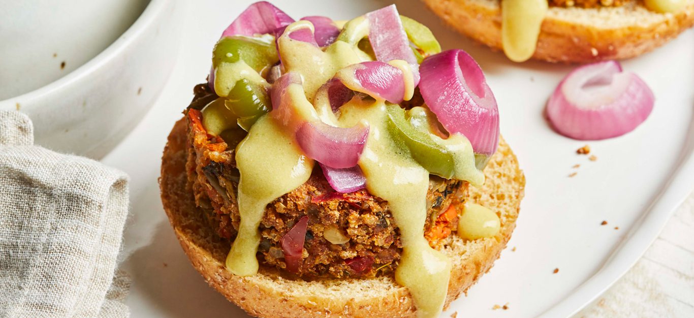 New American Veggie Cheeseburgers topped with a cheesy sauce, jalapenos, and pickled onions on a white plate