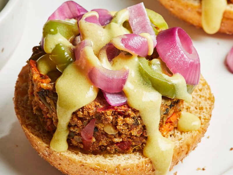 New American Veggie Cheeseburgers topped with a cheesy sauce, jalapenos, and pickled onions on a white plate