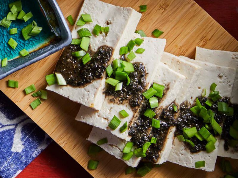 Soft Tofu with Black Sesame and Wasabi Sauce on a wooden cutting board and sprinkled with scallinos