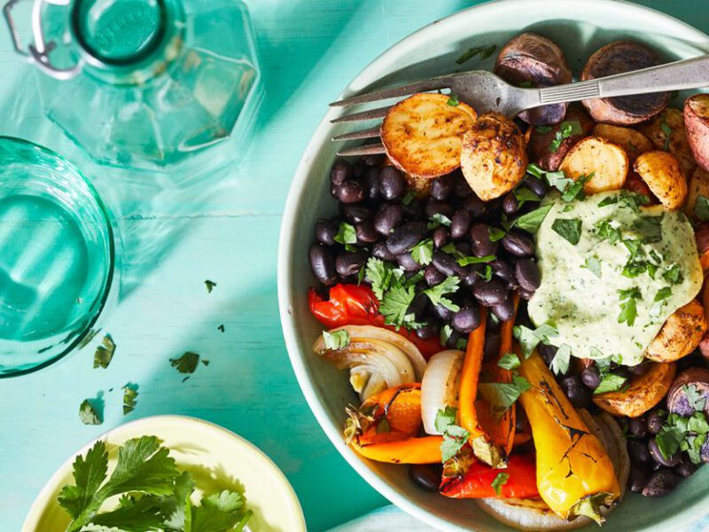 Cilantro-Sauced Roasted Potato Bowl with a sprinkle of fresh cilantro on a blue table with glasses of water