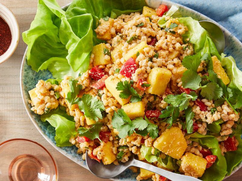 Fresh Pineapple and Barley Salad being tossed with a fork and spoon while sitting on a wood tabletop