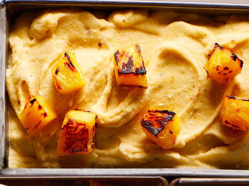 caramelized pineapple nice cream with chunks of toasted pineapple on top in a rectangular metal tin