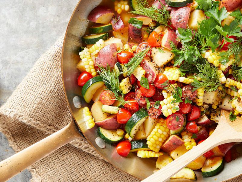 herbed breakfast hash in a metalskillet with a wooden spoon and slices of toasted bread on the side