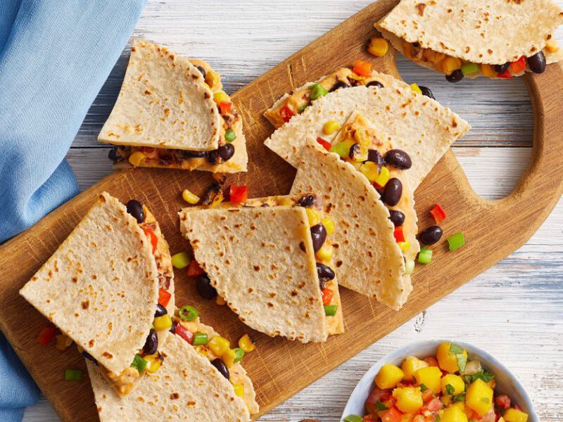 Chipotle Hummus Quesadillas on a wooden serving tray with a bowl of fresh mango salsa