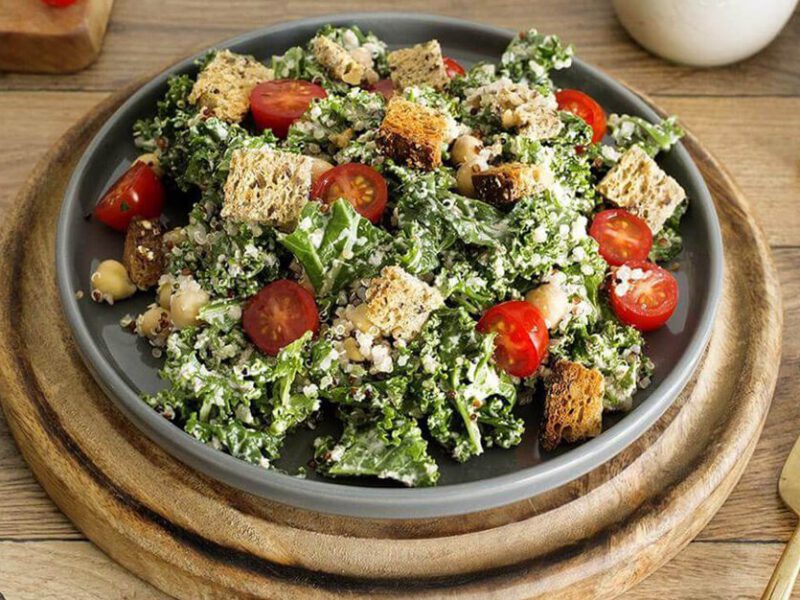 Vegan Kale Caesar Salad in a wooden bowl topped with croutons and tomatoes