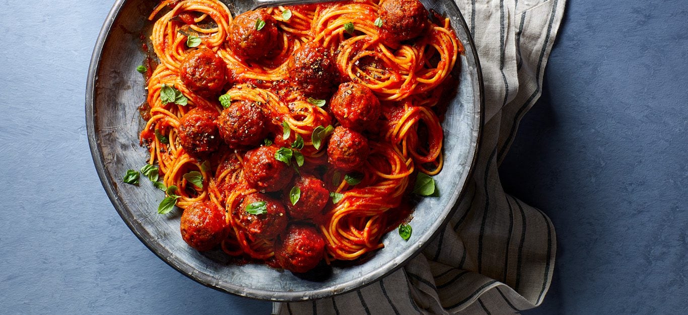 spaghetti marinara with lentil meatballs on a gray ceramic plate on a blue countertop