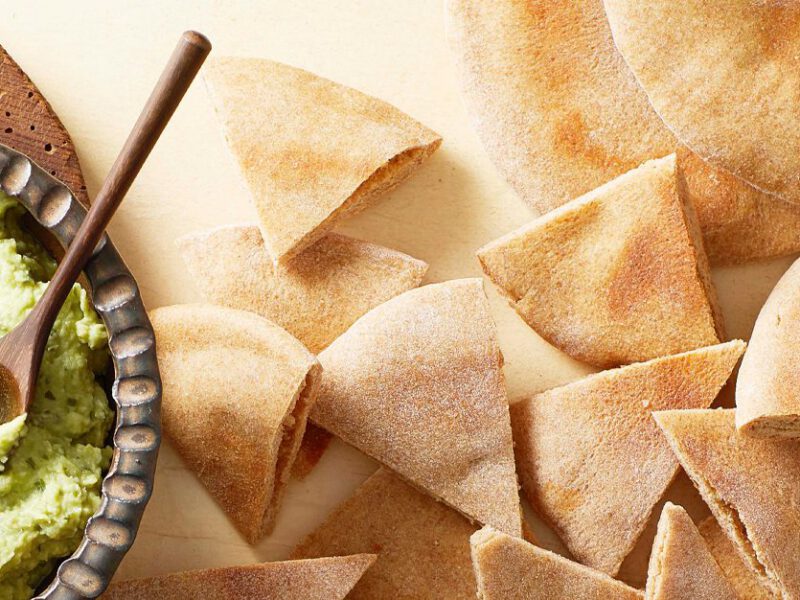 Homemade Vegan Pita Bread cut into triangles on a white counter next to a bowl of green hummus