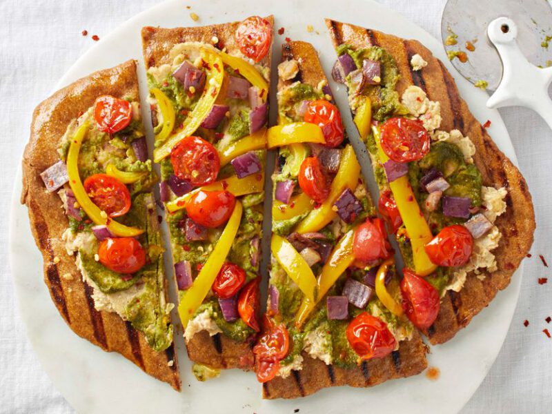 Individual grilled pesto pizzas on a white cloth with a pizza cutter tool
